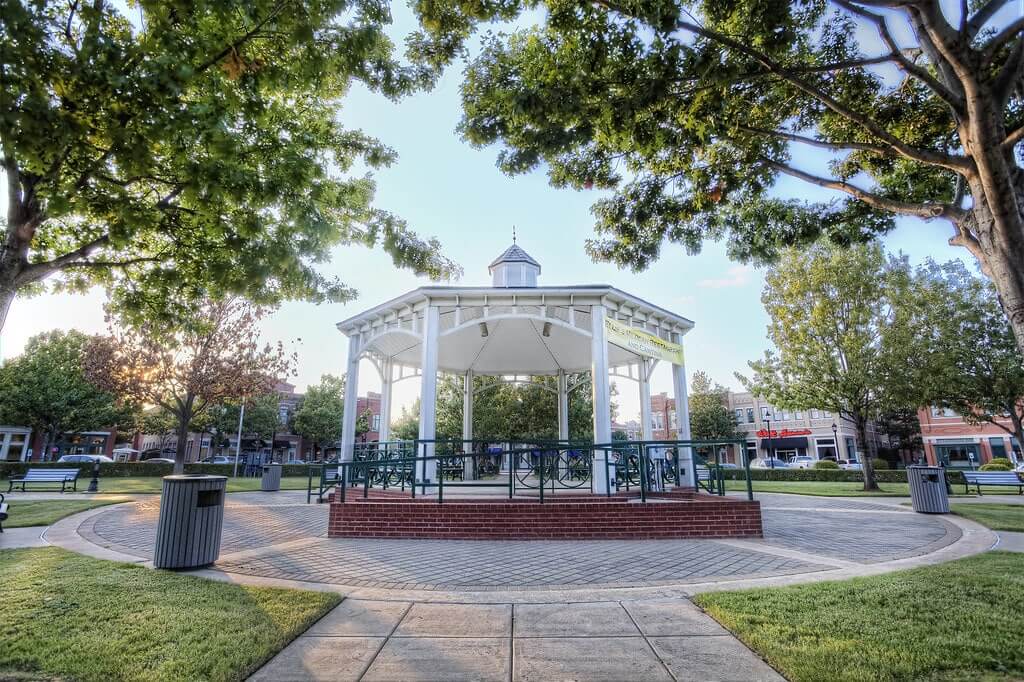 A white gazebo surrounded by trees in a sunny park.